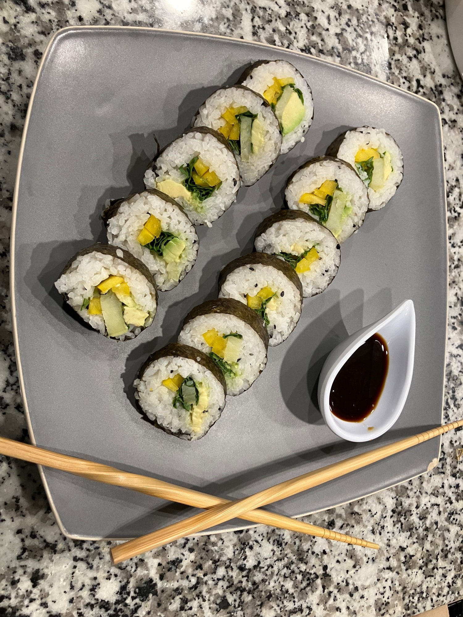 Sushi rolls with avocado, mango and greens on a gray plate with soy sauce and chopsticks