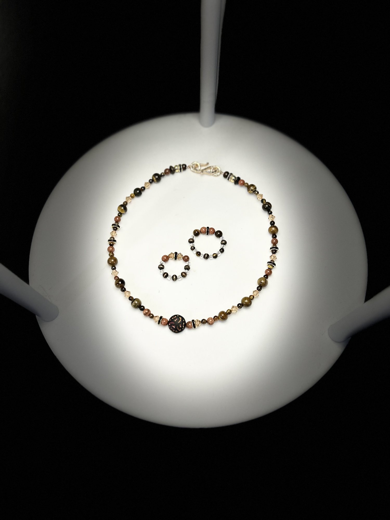 A beaded stone necklace and two beaded rings under a spotlight
