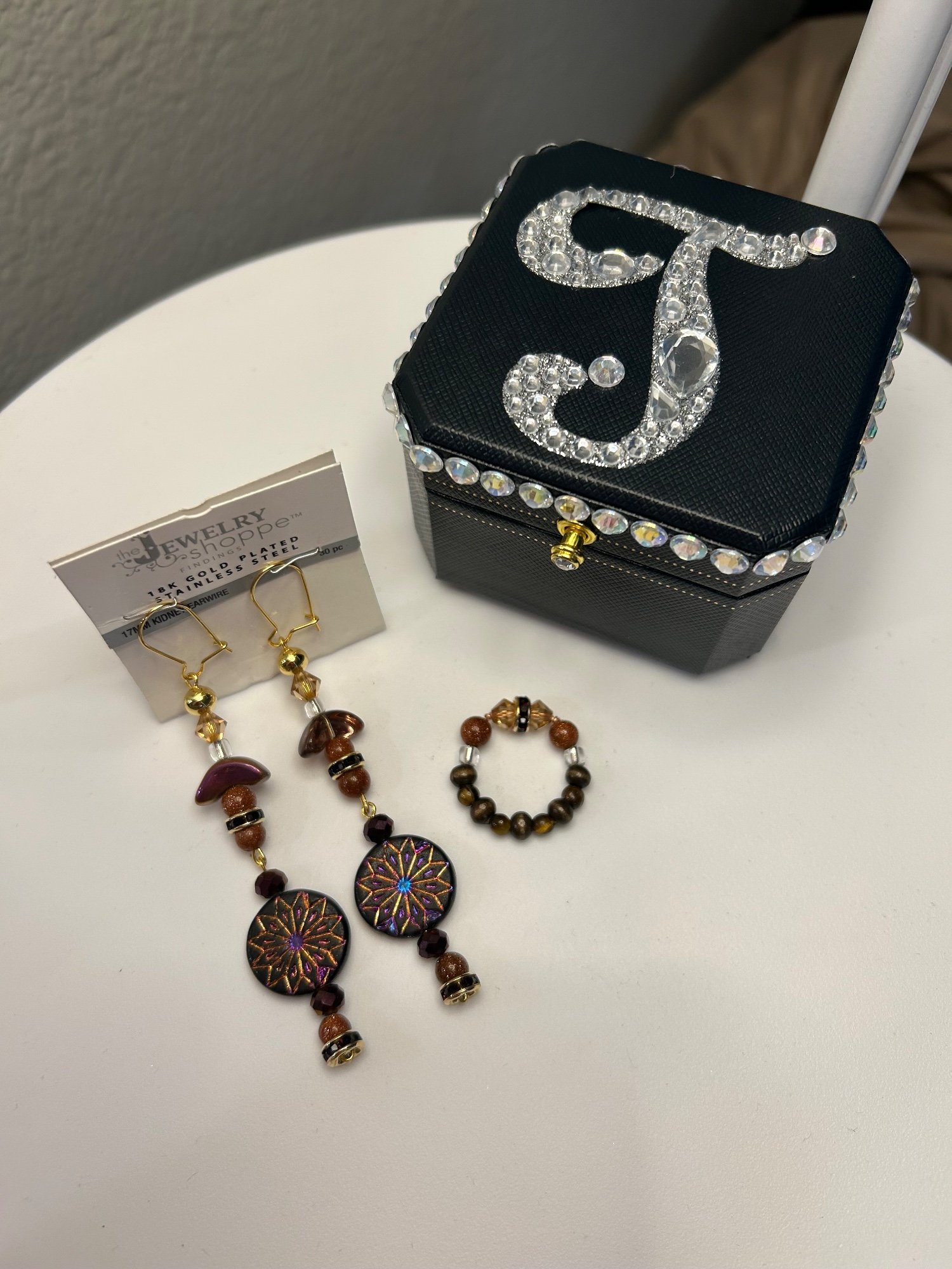 Beaded drop earrings and a beaded ring beside a black jewelry box with a crystal letter T