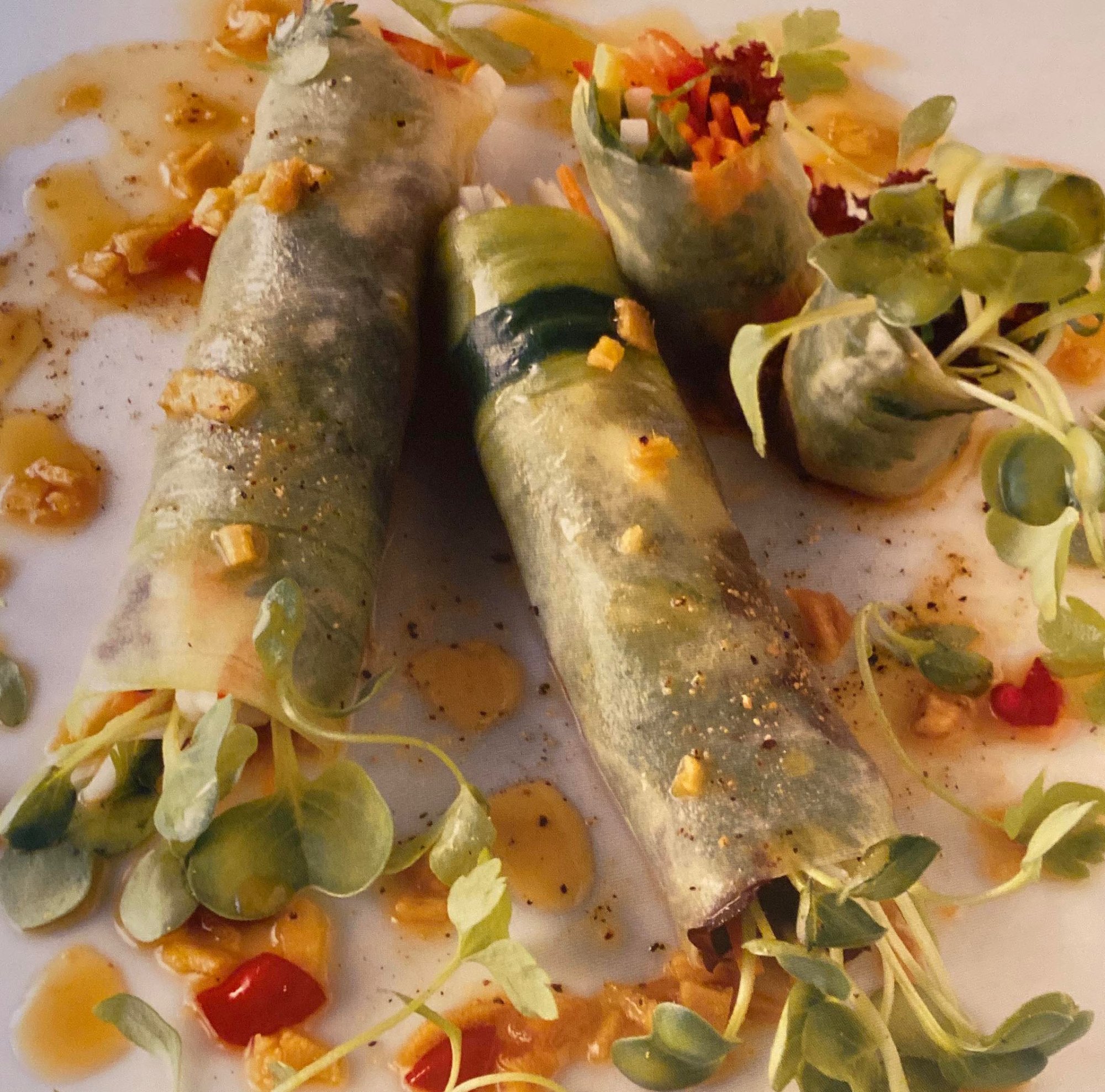 Two fresh rice-paper rolls filled with vegetables, topped with microgreens and a golden sauce