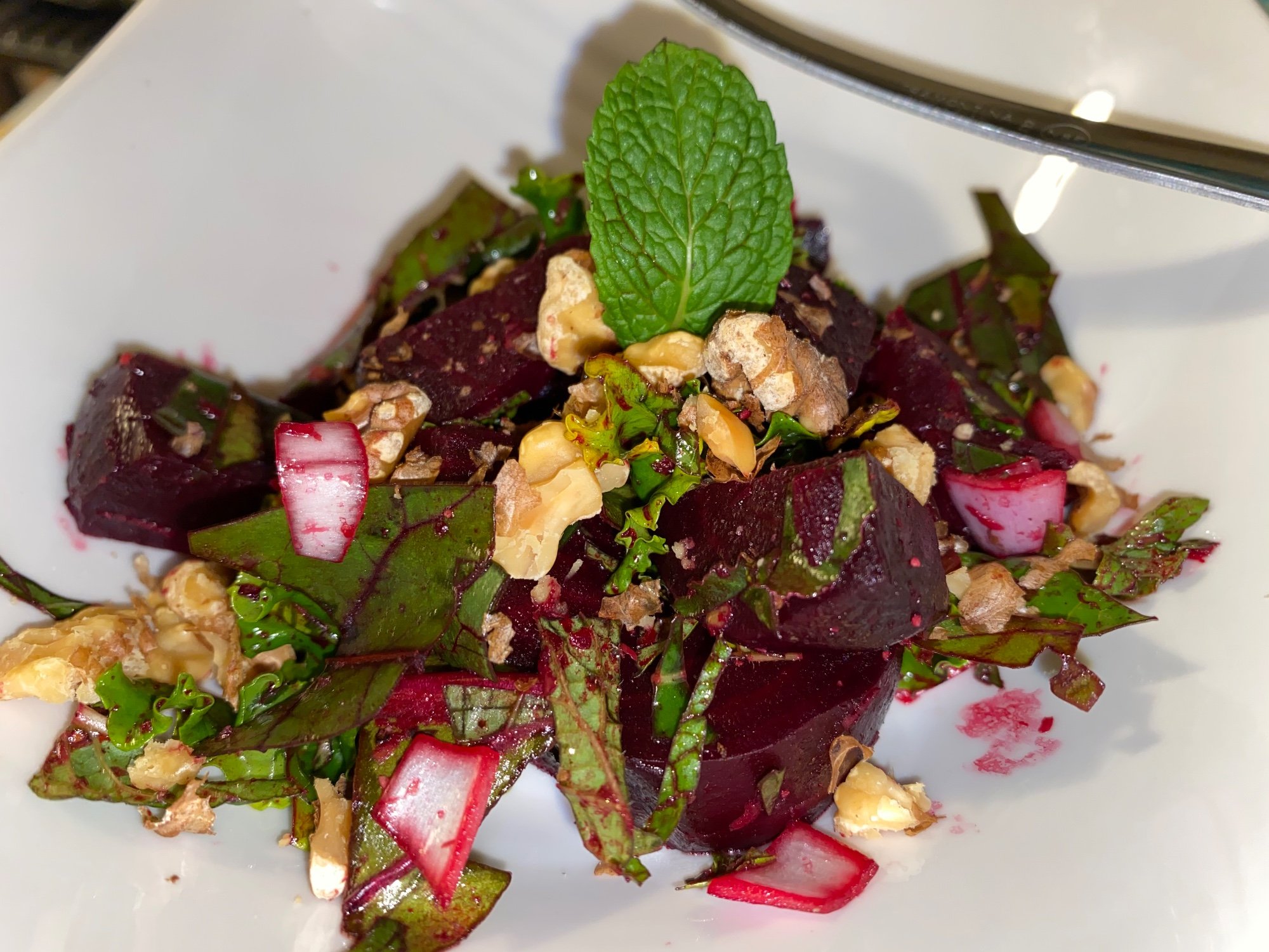 Beet and walnut salad with beet greens, radish and a mint leaf