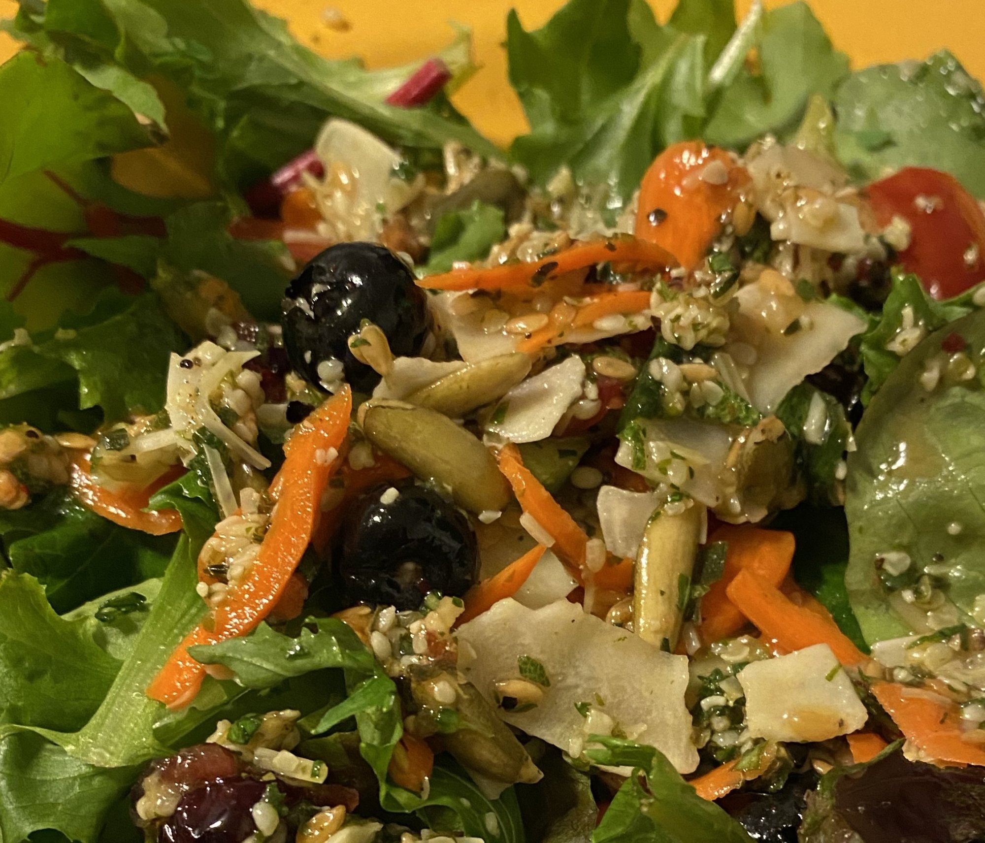 A colorful salad with greens, shredded carrots, olives and seeds