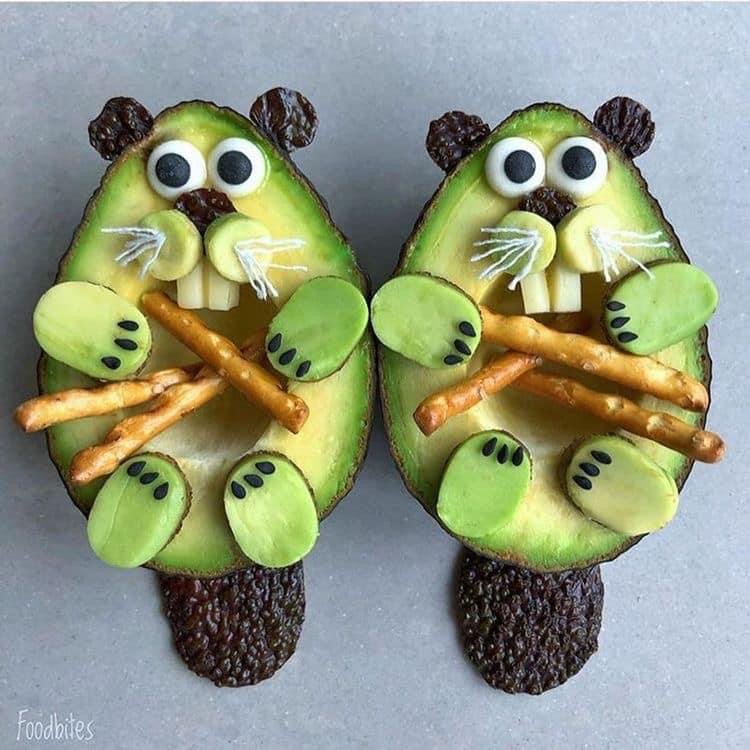 Two avocado halves decorated as beavers with pretzel sticks
