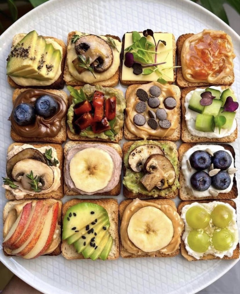 A plate of sixteen small toasts topped with fruit, avocado, mushrooms and spreads