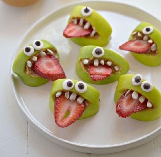 Green apple slices made into smiling monsters with strawberry tongues and candy eyes