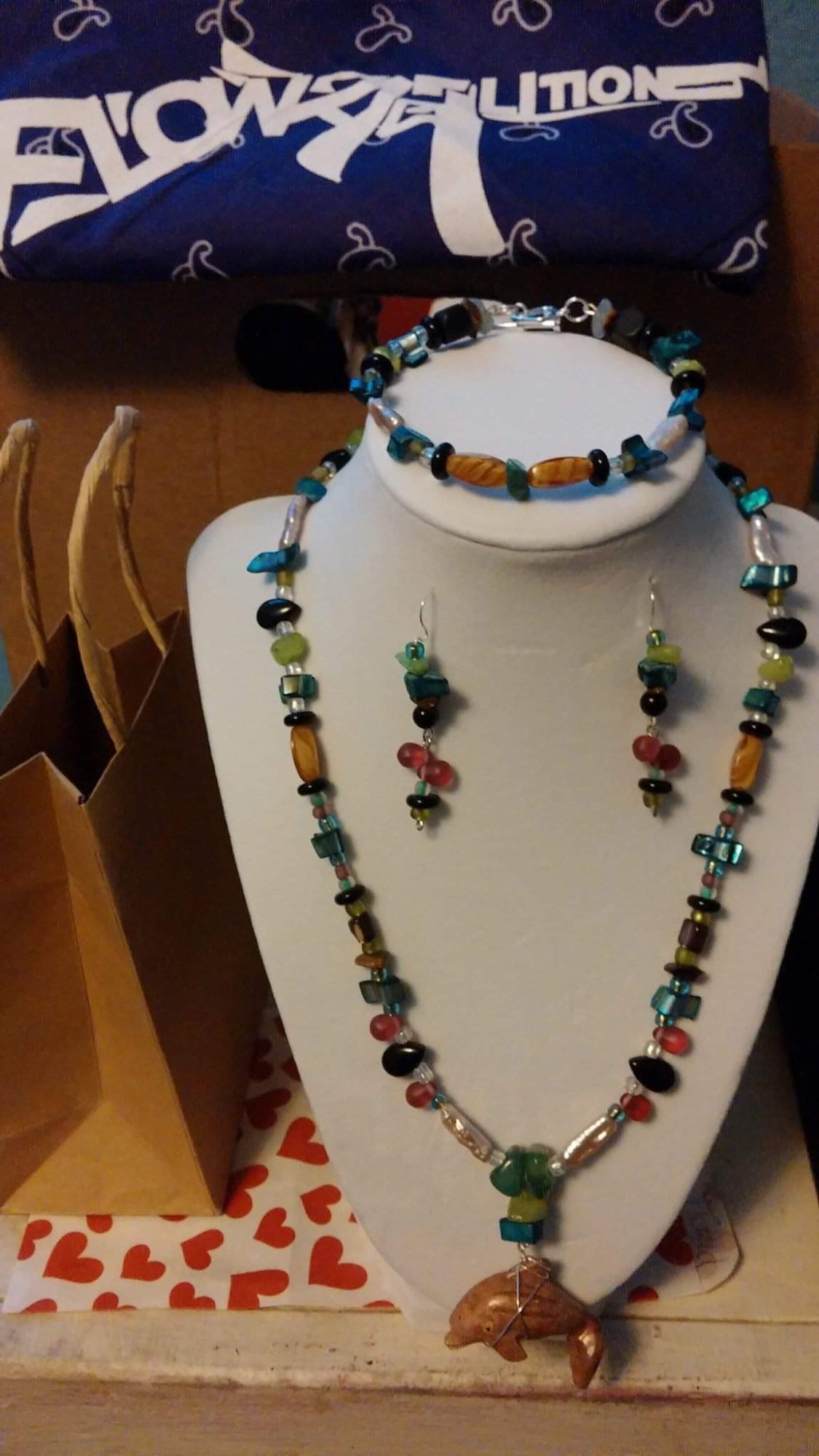 A beaded necklace, bracelet and earrings in teal, amber and green on a black display bust